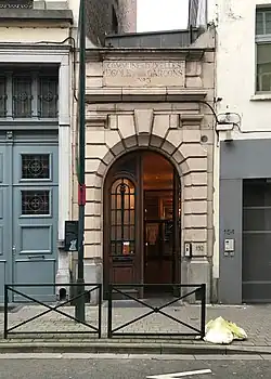 Photographie d'un bâtiment vu depuis la rue, avec un porche en pierre.