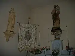 À droite saint Joseph tenant dans ses bras l'Enfant Jésus, à gauche saint Jean l'évangéliste, au centre l'Assomption de Marie broder sur un tissu.