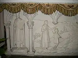 À gauche du bas-relief centrale, un évêque tenant une des tables en pierre de la loi mosaïque