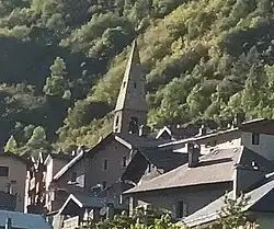 Photographie d'un clocher d'église et des maisons aux toits gris, en tôles ou en pierres, au centre d'un village.