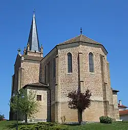 Une église derrière des petits arbres dont le clocher est en arrière-plan à gauche et le chœur en premier plan à droite.