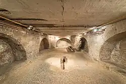 Photographie d'une large pièce souterraine au centre de laquelle se trouve une tombe creusée dans le sol et entourée par plusieurs voûtes.