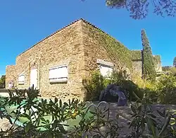 Cliché de bâtiment. Devant façade, piscine rectangulaire avec pont-levis. En angle, statue de couple nu enlacé.
