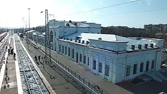 Photographie prise depuis une passerelle piéton au-dessus de vois ferroviaires prenant un bâtiment blanc à côté de quais de gare