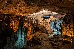 Une grotte éclairée de lumières ocres et bleues. Une sorte de plafond, des éboulis sur une sorte de sol, l'ensemble rocailleux et terreux.