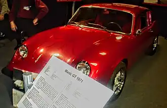 Une petite voiture rouge dans une salle d'exposition. Au premier plan, un écriteau où il est inscrit «&nbsp;Manic GT 1971&nbsp;».