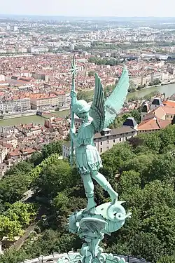 Statue de l'archange Michel frappant le dragon ; en arrière-plan, le sud de l'agglomération lyonnaise.