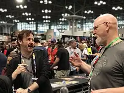 Un homme barbu discutant avec un homme chauve.