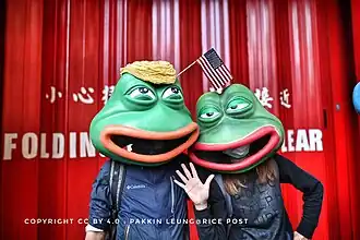 Personnes déguisées avec des masques de Pepe la grenouille ; celle portant une perruque blonde représente Donald Trump.