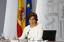 Photographie d'une femme, assise à un bureau vêtue de blanc.
