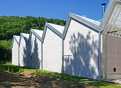 Ancien bâtiment industriel à shed peint en blanc surmonté d'une petite cheminé en métal.