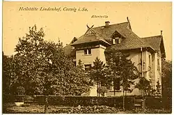 Carte postale d'une villa bourgeoise, à la façade claire, assez opulente, mais sobre, avec plusieurs pas de toits en tuiles, et entourée d'une haie, vue depuis un jardin.