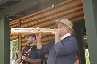 L'artiste Jocelyn Maltais du collectif Interaction Qui soufflant dans l'Arbre Flûte lors de l'exécution de l'action performative Pierres Bûchées.