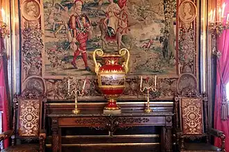 Photographie en couleur d'un vase posé devant une tapisserie.