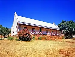 Photographie d'une maison blanche avec une grande terrasse abritée dans un paysage steppique.