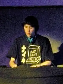 A. G. Cook, casque de DJ autour du cou, mixant.