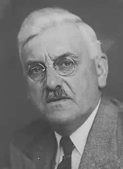 Photographie noir et blanc d'un homme moustachu en buste, de face.