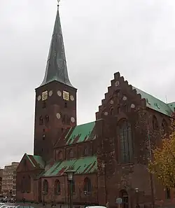 Photo représentant une cathédrale en brique rouge aux toits verdâtres.