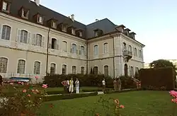 Photographie couleur d'un bâtiment de style classique, devant lequel des visiteurs se promènent dans un jardin.