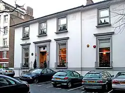 Photographie en couleur d'une façade d'immeuble avec plusieurs voitures garées au premier plan.