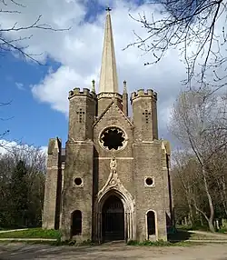 Chapelle en arrière plan entourée d'arbres et de feuilles mortes, image en couleur.