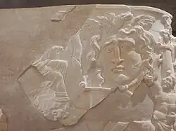 Gorgone du côté droit, jambes d'un personnage assis.