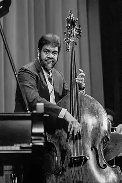 Un homme derrière un piano joue de la contrebasse.