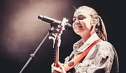 Photographie d'une jeune femme chantant devant un micro dans une salle de concert.
