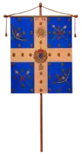 Image montrant un drapeau accroché à une hampe, il se compose d'une croix blanche encadrée de quatre carrés bleus.
