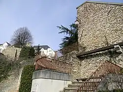 Hauts murs de pierres appareillées, parcourus par un escalier à rambarde en fer forgé.