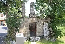 Photographie en couleurs d'un bâtiment en ruines à demi masqué par la végétation.