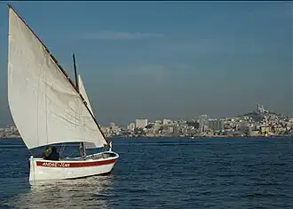 Petit bateau en bois avec une voile triangulaire, sur la mer