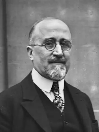 Portrait photographique en noir et blanc d'un homme souriant légèrement, portant des lunettes rondes.