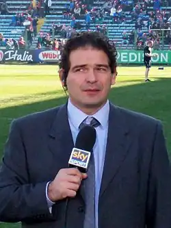 Photo en buste d'un homme en costume tenant un microphone et portant une oreillette