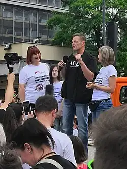  Photo en couleur d'un homme aux cheveux courts châtains parlant dans un micro