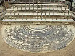 Une pierre de lune au pied d'un escalier de pierre aux contre-marches décorées de nains.