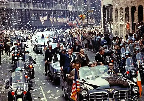 Photographie en couleur de l'équipage d'Apollo 11 lors d'une parade véhiculée en ville.