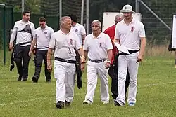 Photo montrant des hommes habillés en blanc marchant sur une pelouse.