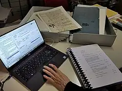 Photographie couleur d'un ordinateur et de registres avec boites d'archives