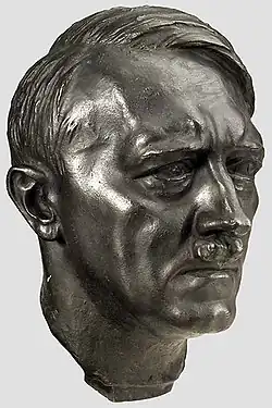 Photo en couleurs (fond gris clair) d'une tête en bronze d'Adolf Hitler, réalisée par le sculpteur Arno Beker, en 1398.
