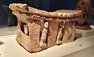 Objet en terre cuite dont la partie supérieure est incurvée, à base rectangulaire décorée de personnages.