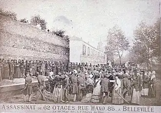 Une foule d'otages se tenant sur une estrade, devant un mur, face à un peloton d'exécution.