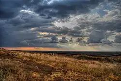 Paysage automnal avec herbe jaunie et soleil entre les nuages