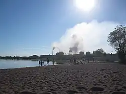 Une plage en avant plan et une usine au fond.
