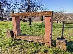 Photo d'un banc en gré rose des Vosges, le banc dispose de deux traverses superposées, la traverse du haut situé à plus d'un mètre de hauteur est gravé de l'année 1854.