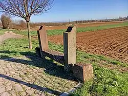 Photo d'un banc-reposoir en gré rose des Vosges, les pieds sur les coté remontent jusqu'à un mètre avec un accotoir incurvé.