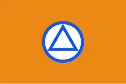 Reproduction en couleurs de l'emblème du VNV. Sur un fond orange, un triangle aux contours bleu est inséré dans un cercle blanc