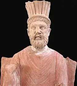 Vue partielle d'une statue représentant un homme barbu assis sur un trône.