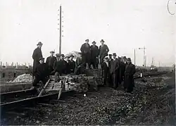Photo en noir et blanc d'une barricade barrant une voix ferrée et sur laquelle pose un groupe d'hommes majoritairement en costume de ville