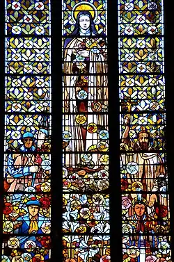 Élément de vitrail. En haut et au centre de l'image, une femme avec une auréole porte une croix et lance des roses. En bas à gauche de l'image, un poilu de la Grande surmonte un marin en train de prier. À leur droite, un homme barbu tonsuré surmonte une femme à la peau mate en train de prier.